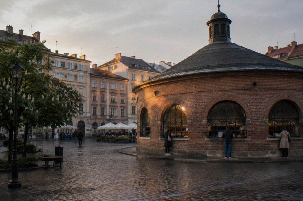 Brick rotunda market building on a wet cobbled square with pastel tenements and a few distant people at the windows.