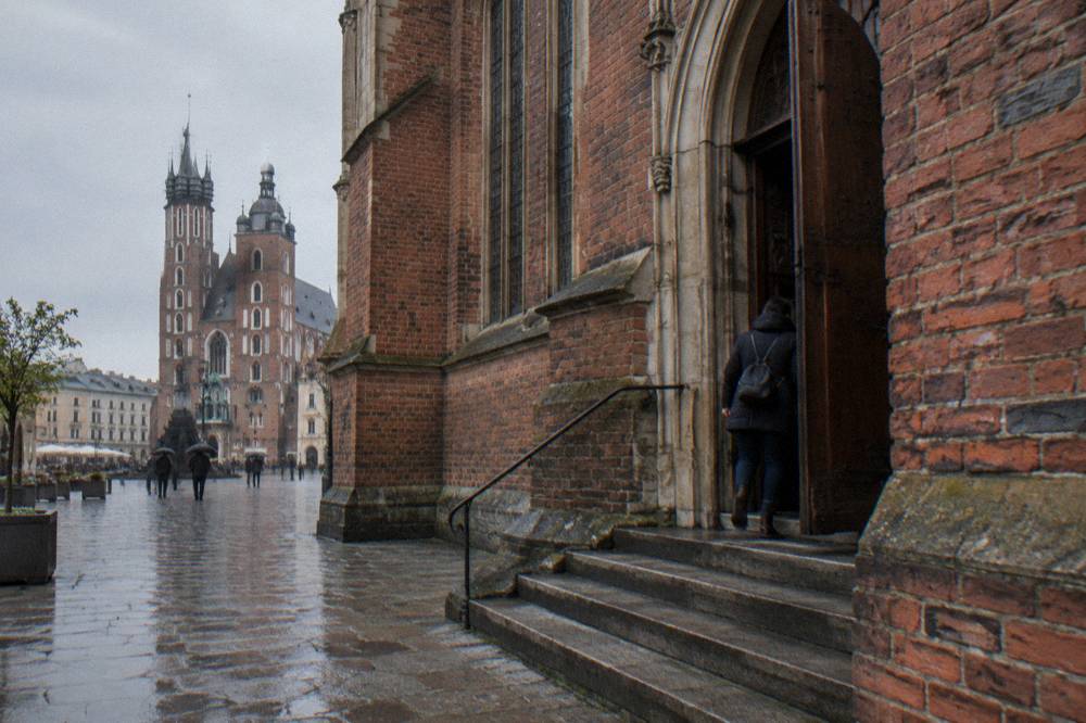 Wet stone steps lead to a side door in a red brick Gothic church, with St Mary's Basilica towers across the square.