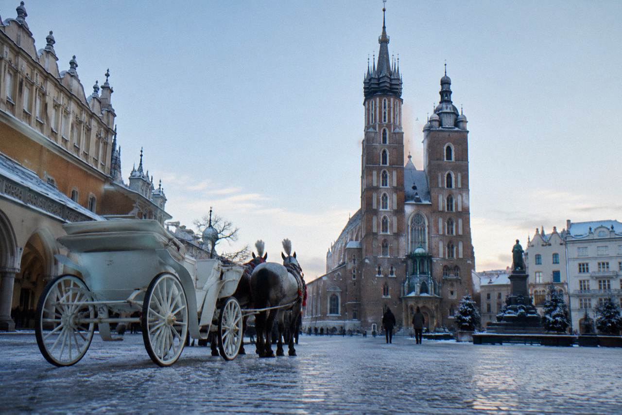Snowy cobbled square with a horse carriage facing the twin brick towers of St Mary's Basilica in Krakow.
