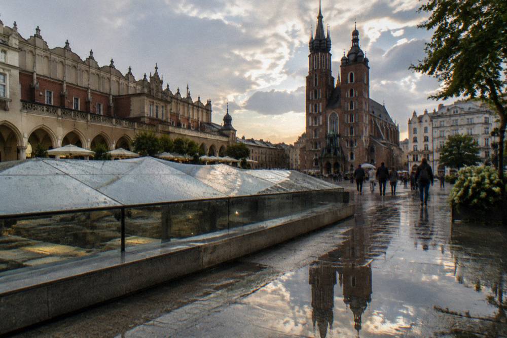Wet paving reflects St Mary's Basilica beside the glass roof of the Rynek Underground pavilion on Krakow's Main Market Square.