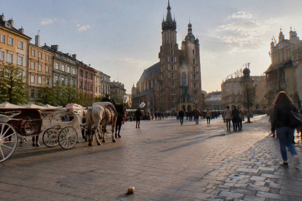 Plaza del mercado empedrada con carruajes de caballos, peatones a lo lejos y las dos torres gemelas de ladrillo de la basílica de Santa María bajo la luz del atardecer.