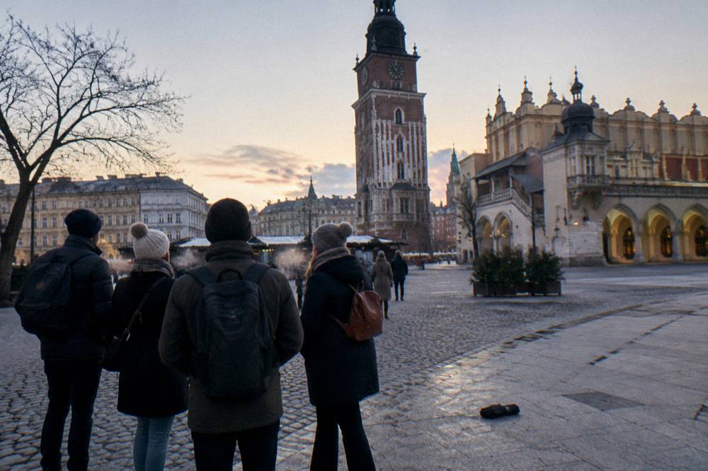 Grupo de free tour en invierno de pie sobre los adoquines de la Plaza del Mercado de Cracovia, cerca de la Torre del Ayuntamiento y la Sala de Comercio al atardecer.
