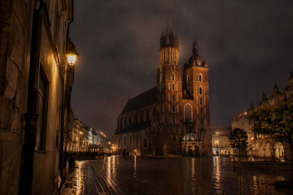 Los adoquines mojados reflejan las farolas mientras la basílica de Santa María se alza sobre una Plaza del Mercado de Cracovia vacía de noche.