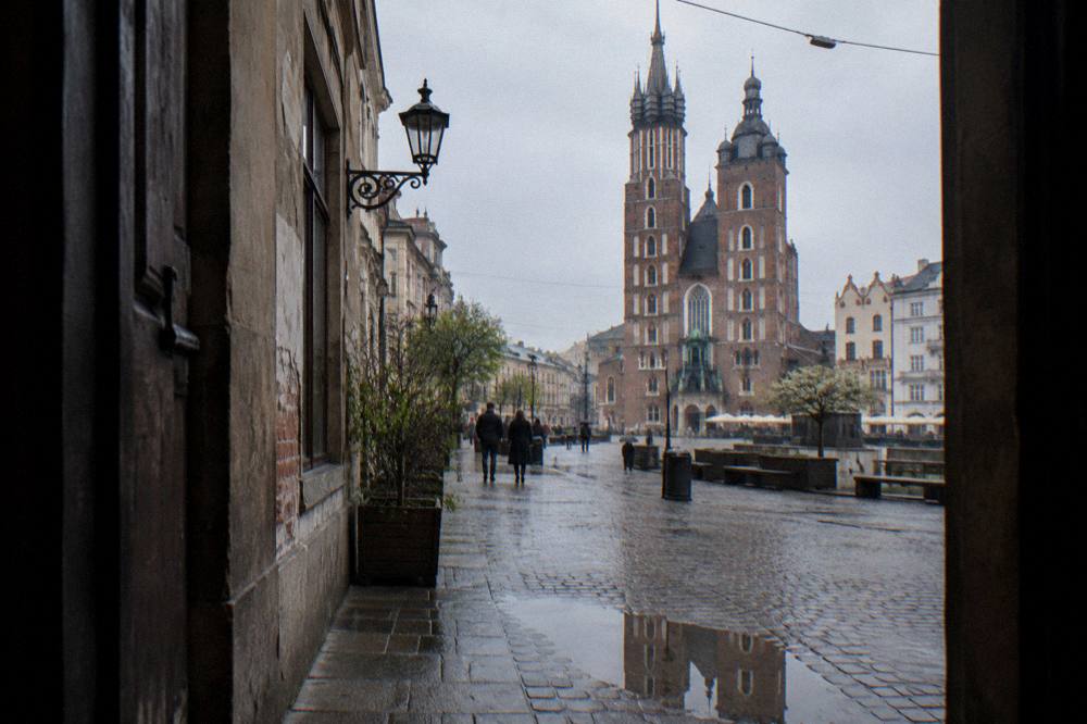 Calle empedrada mojada vista desde una puerta, que lleva hacia las dos torres gemelas de ladrillo de la basílica de Santa María en el Casco Antiguo de Cracovia.