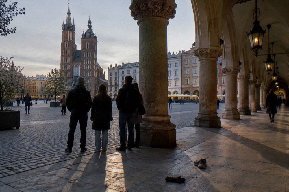 Grupo reducido sobre adoquines bajo las galerías de la Sala de Comercio con la basílica de Santa María al fondo en la Plaza del Mercado de Cracovia.
