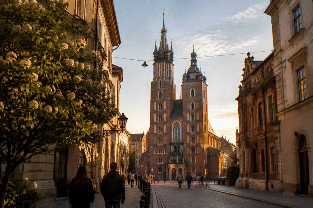 Dos personas caminan por una calle empedrada hacia las torres gemelas de la basílica de Santa María con la luz cálida del atardecer.