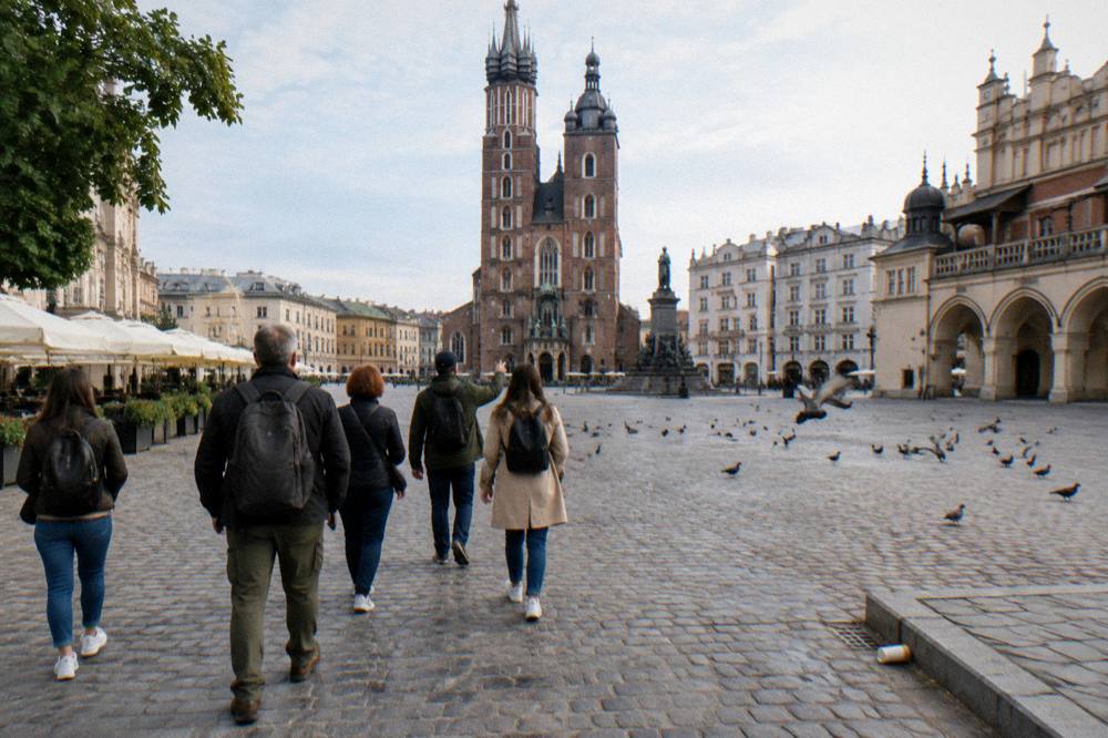 Small group walks across Krakow Main Market Square toward St Mary's Basilica as pigeons scatter on the cobbles.